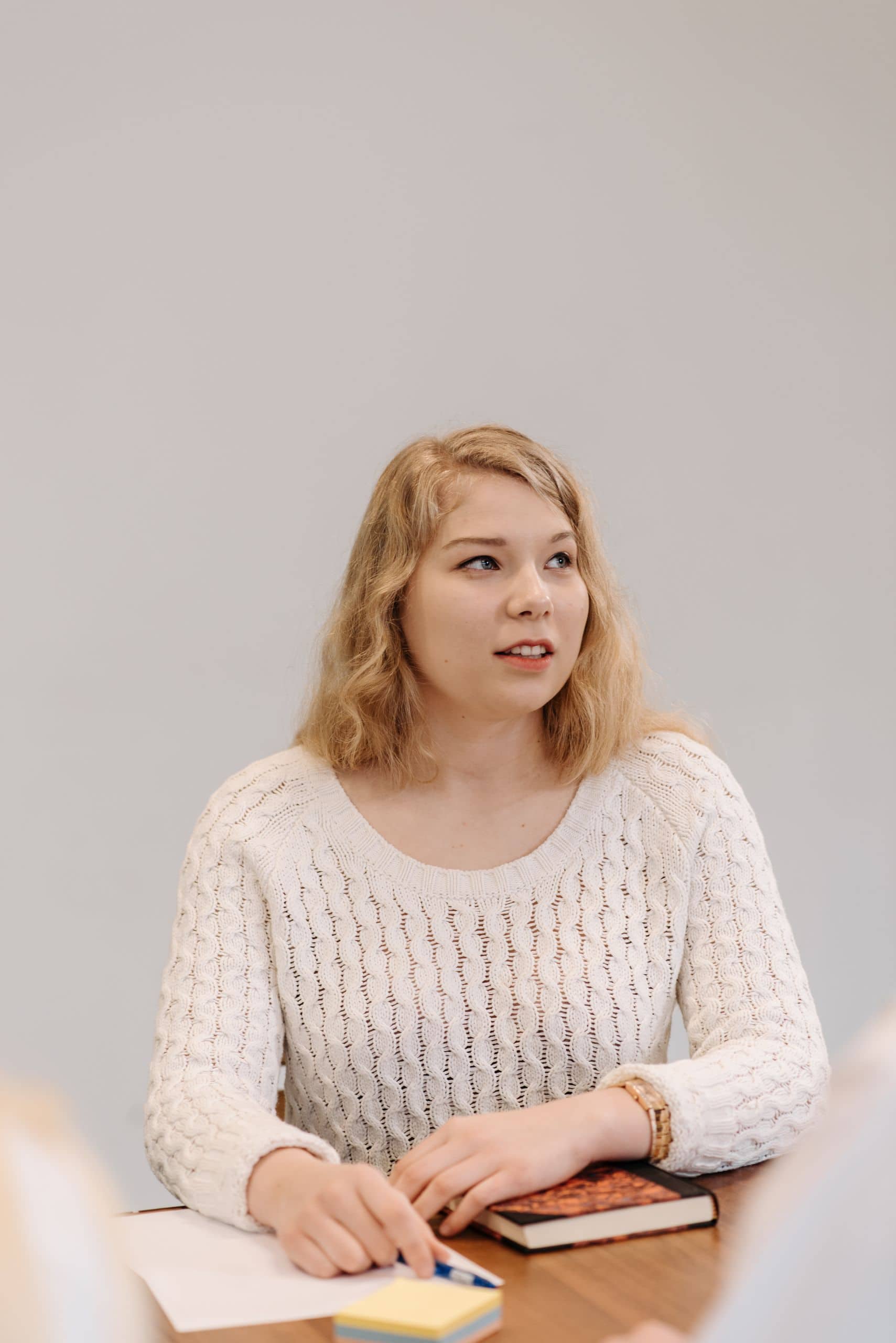 Angebot 9 A young woman in an office setting wearing a white sweater at a meeting table.