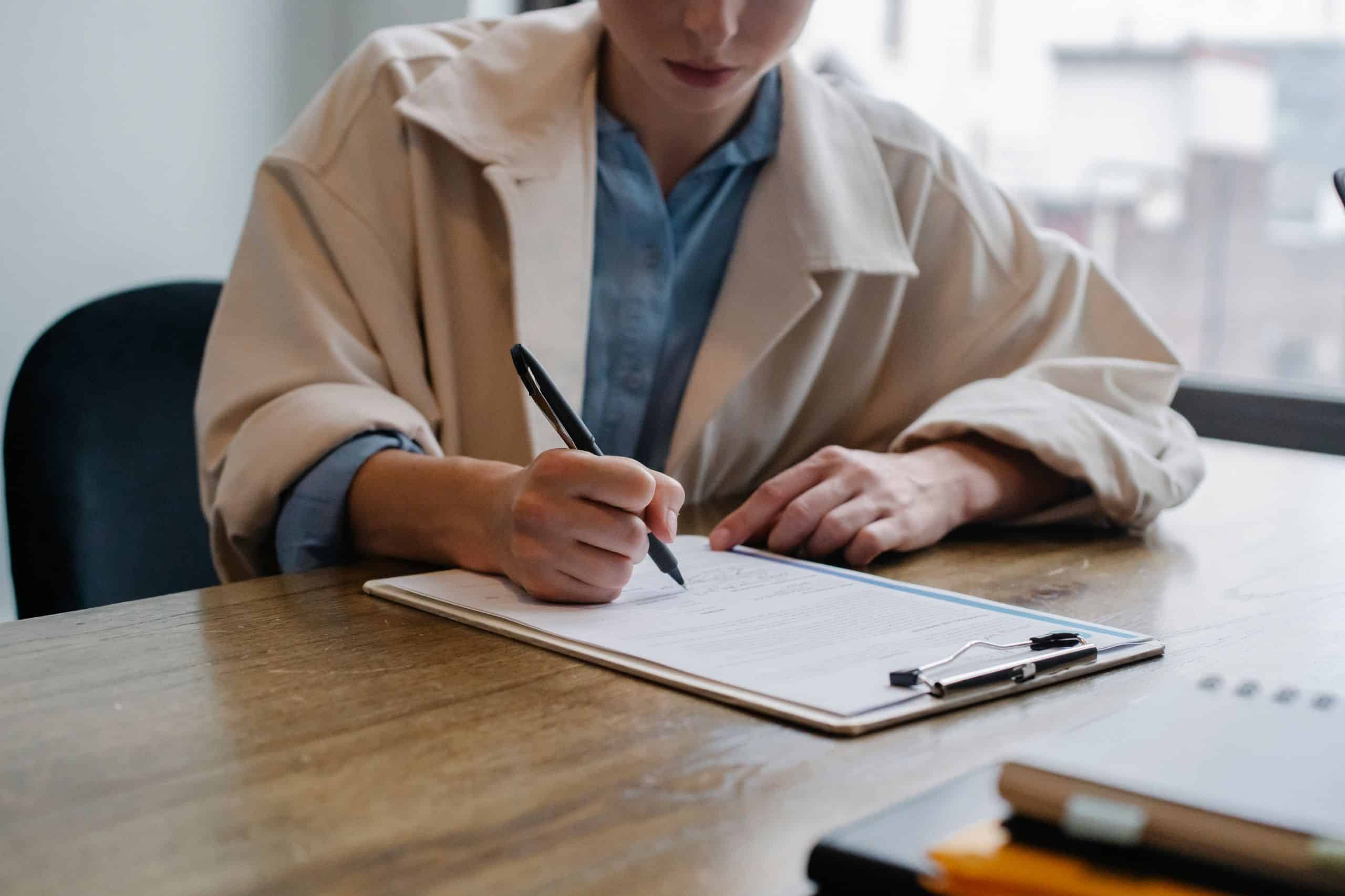 Angebot 10 Crop young female unemployed job seeker filling questionnaire sitting at table during interview in office